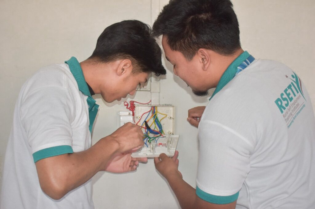 Two vocational trainees practising electrical wiring skills during a hands-on practical assessment session at a skill training centre in India