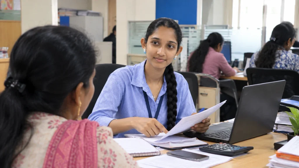 Young Indian woman working as a relationship manager, assisting a customer with financial documents in an office.